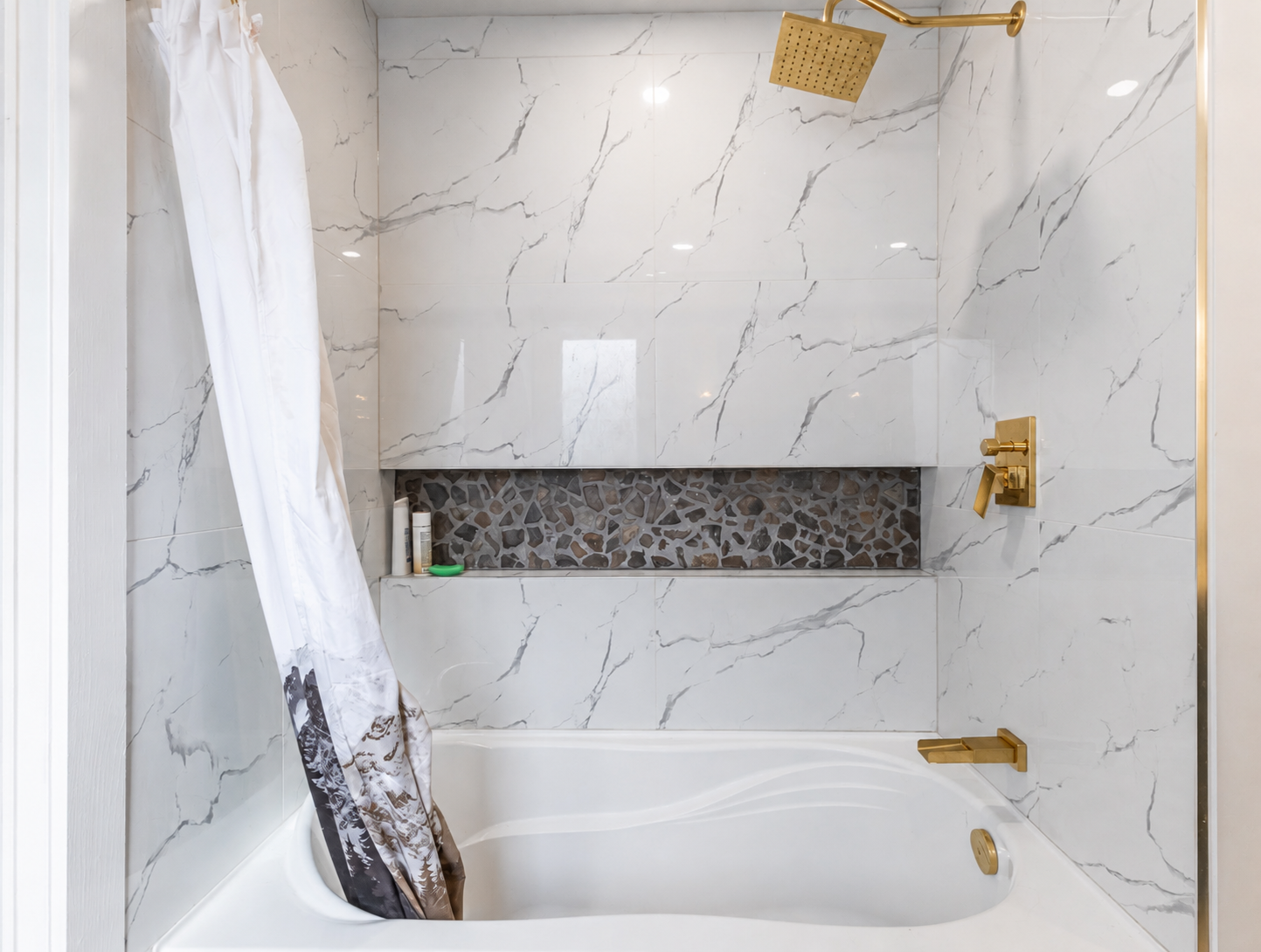 Finished marble tub and shower with brushed gold fixtures and a river stone niche