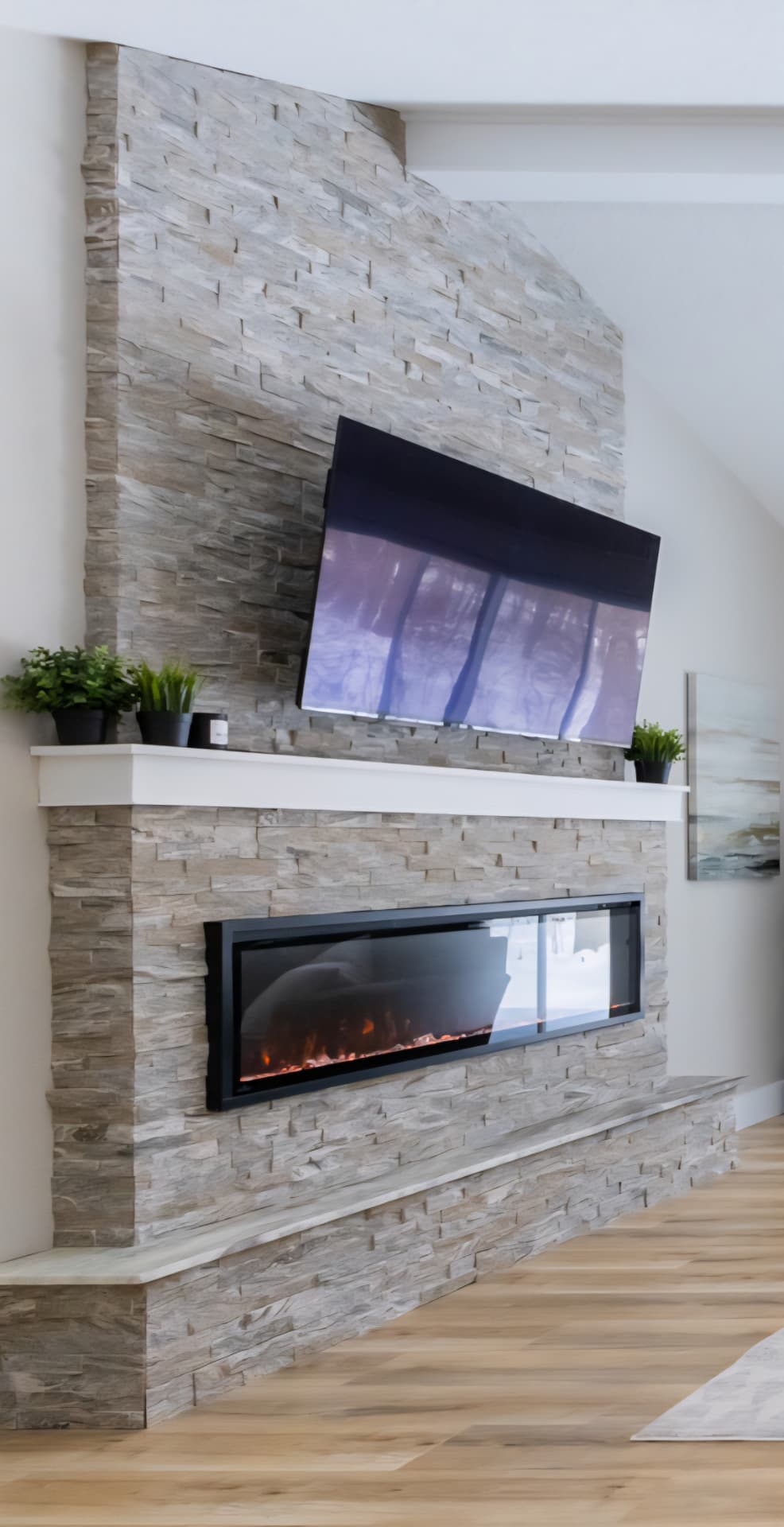 Finished floor-to-ceiling stacked stone fireplace with linear electric insert, white mantel and mounted television
