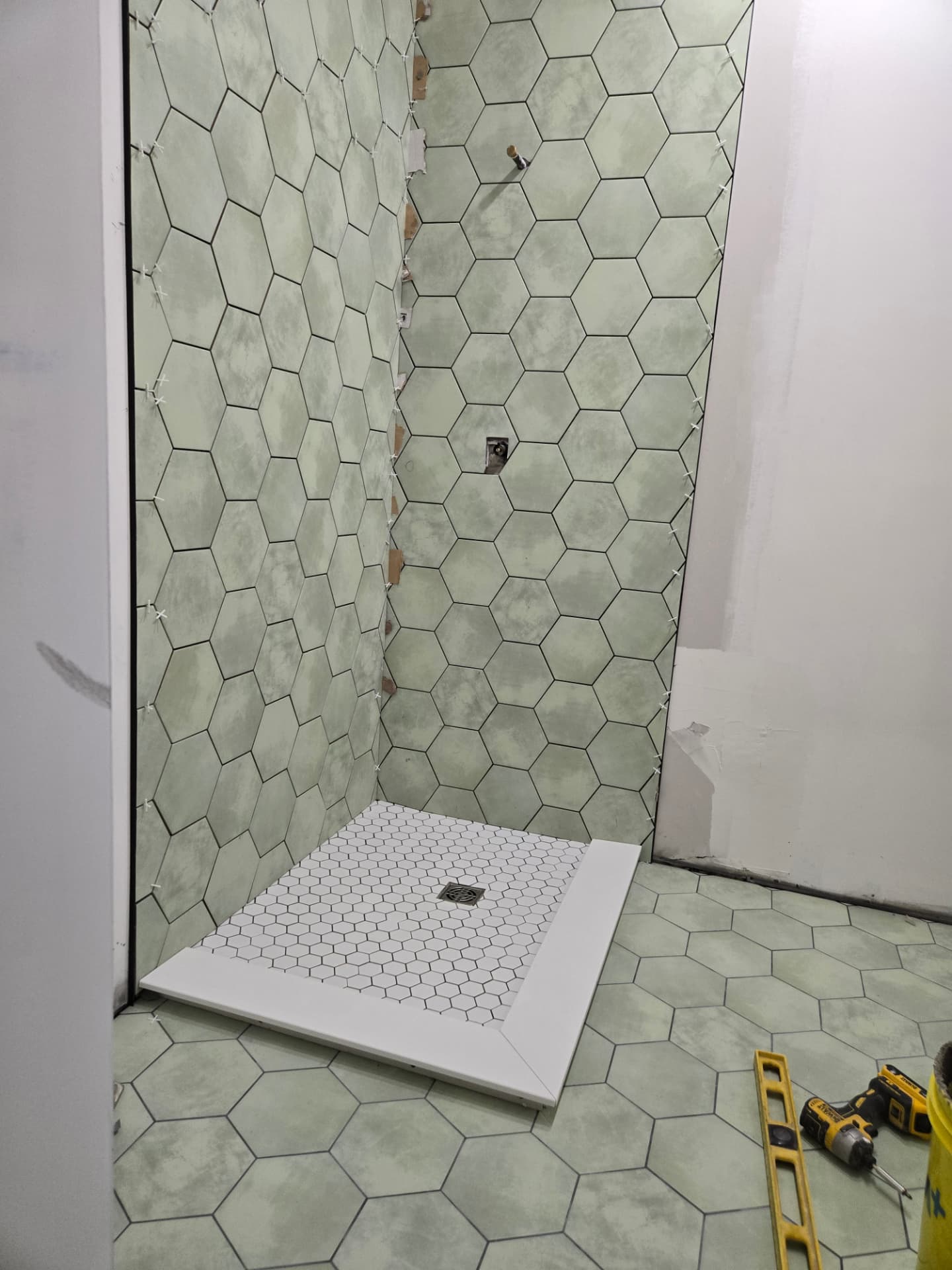 Large sage hexagon tile installed on the shower walls with the white mosaic shower base