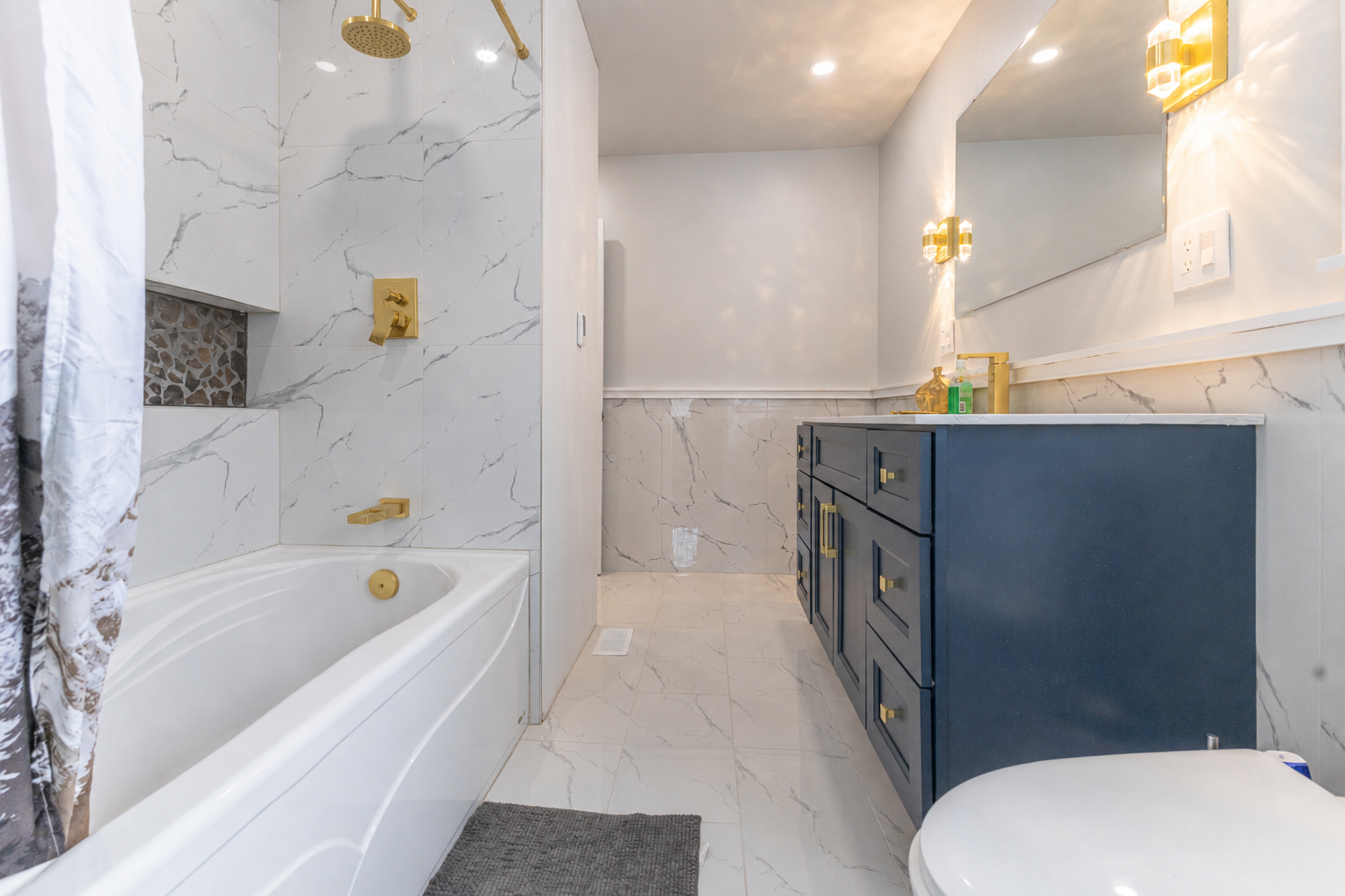 Completed bathroom with navy vanity, gold sconces and marble tile throughout