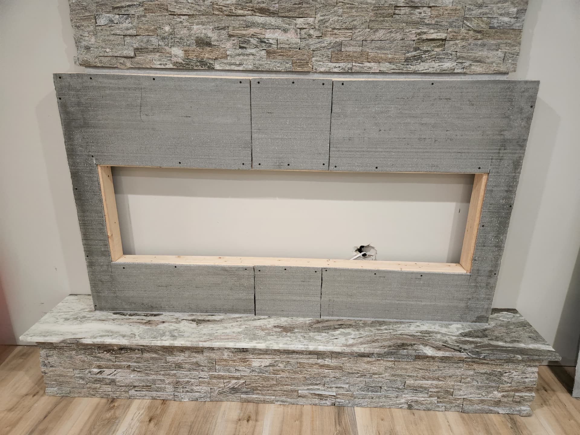Linear fireplace surround framed and backer-boarded with the stacked stone hearth and quartz bench in place