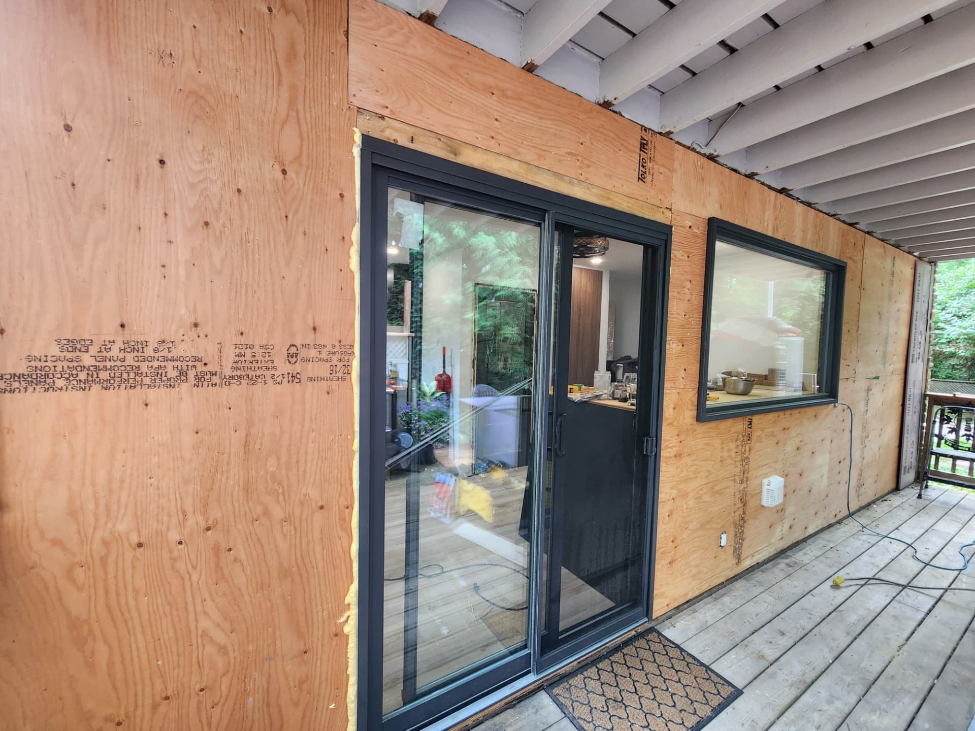 New patio slider and picture window set into fresh plywood sheathing on the covered deck wall