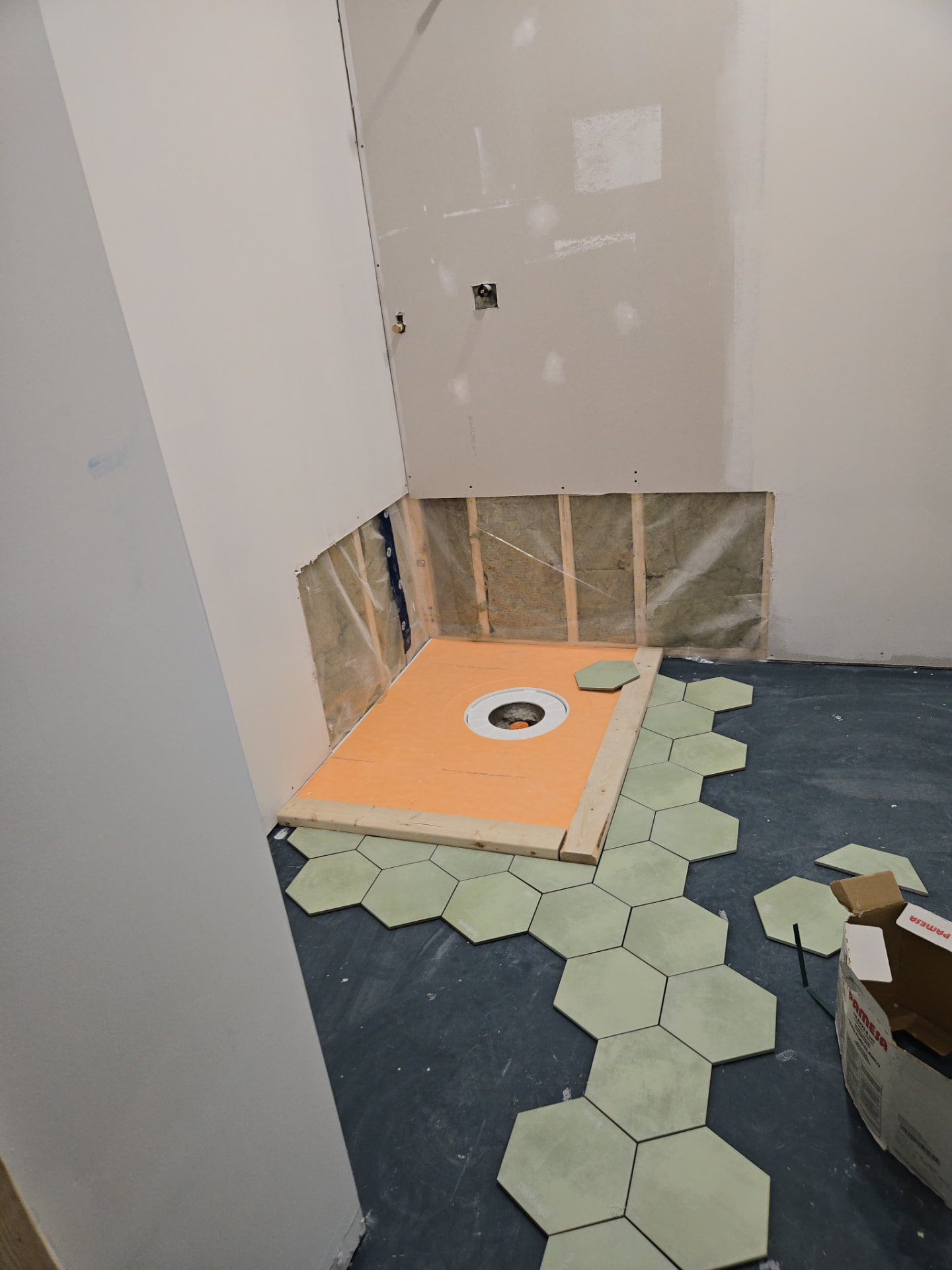 Sloped shower pan and drain set in place as the sage hexagon floor tile is laid out