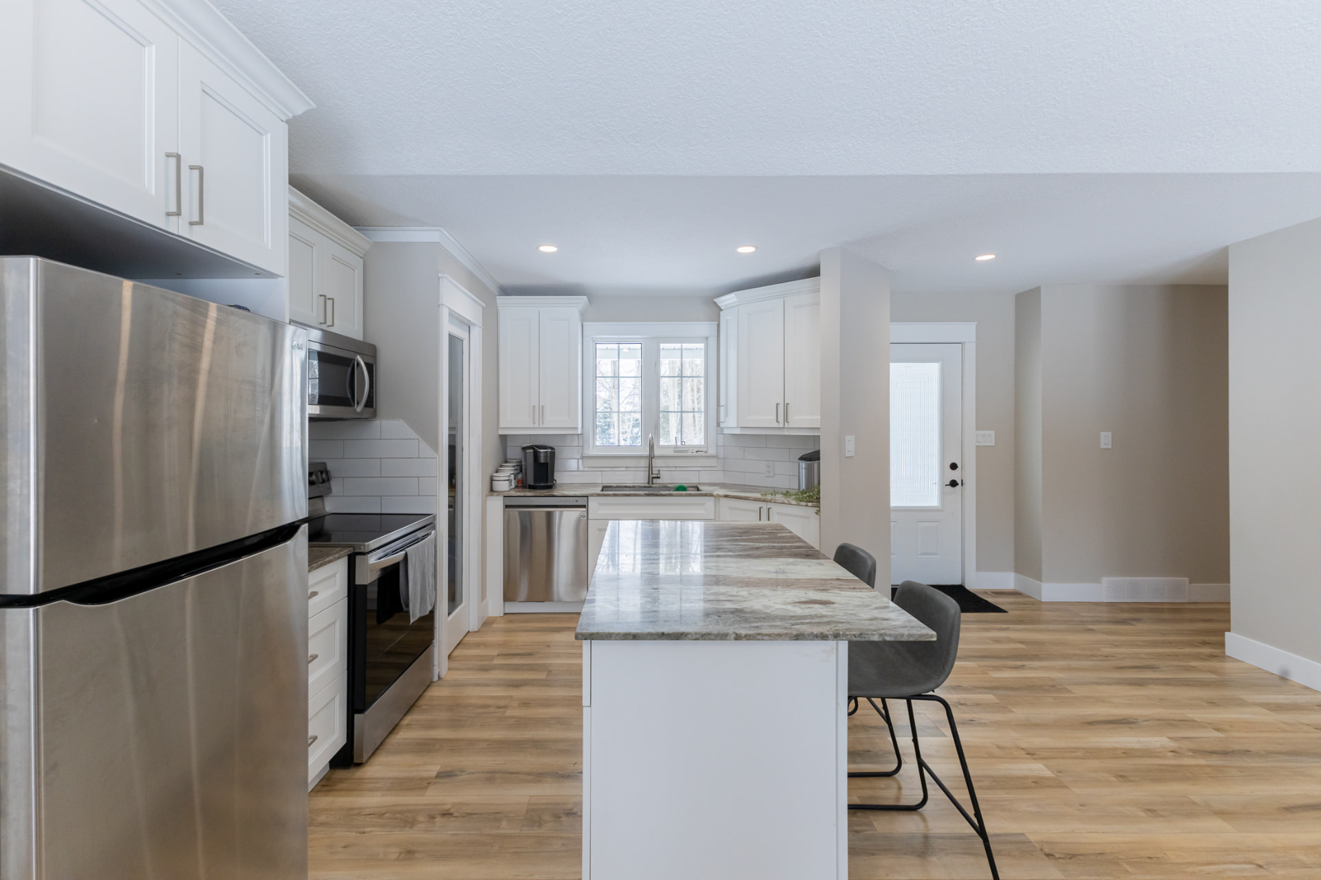 Galley view of the finished white kitchen with wide-plank flooring and pantry door